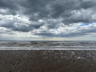Crosby Beach with wet sand, a glimpse of the sea, and a dramatic overcast sky. Liverpool,...