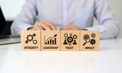 Four wooden blocks representing key business concepts integrity with gears leadership with a growth chart trust with people and gears and impact with a magnifying glass and gears