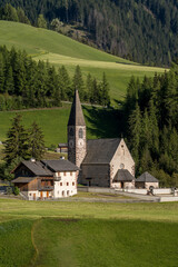 Close-up view of Santa Maddalena Church in the green valley of South Tyrol with forested hills in the background.
