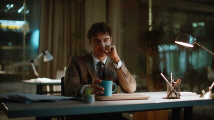Businessman drinking coffee night office closeup. Smiling overtime worker break