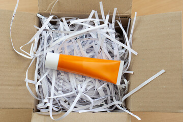 A orange product tube nestled among shredded white paper inside a brown cardboard box, signifying...