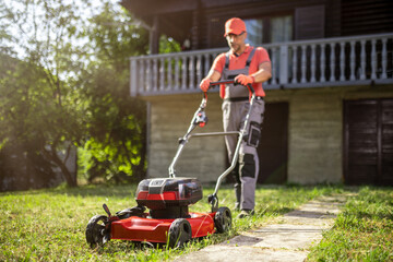 Fototapeta premium Man mowing the lawn in front of a house on a sunny day, showcasing outdoor maintenance skills and home care