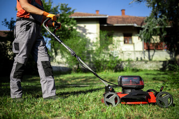 Gardener uses electric mower to maintain green lawn in sunny backyard on a clear day