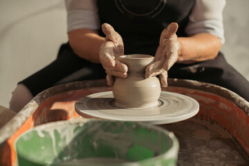 Potter creating clay vase on pottery wheel: senior woman making ceramics