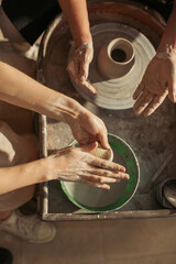 Potter working clay on pottery wheel during lesson with senior woman