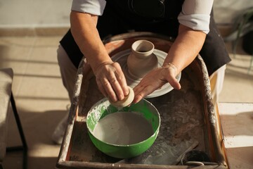 Potter cleaning sponge in water before smoothing clay vase on pottery wheel