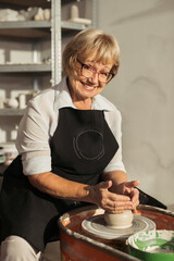 Senior woman making pottery on potter's wheel in workshop