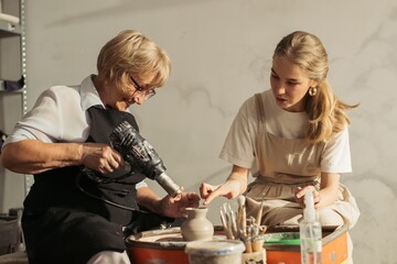 Senior woman learning pottery with heat gun and teacher guidance