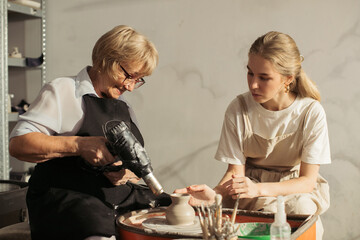 Senior woman using heat gun in pottery class with teacher
