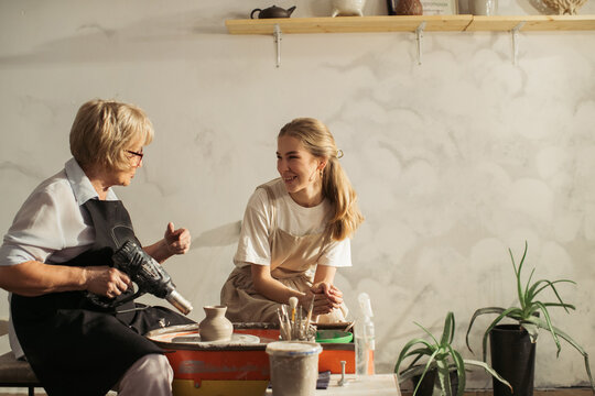 Senior ceramist drying a clay vase with heat gun during pottery class - Powered by Adobe