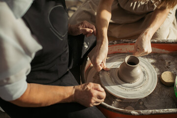 Potter assisting senior woman creating clay vase on pottery wheel