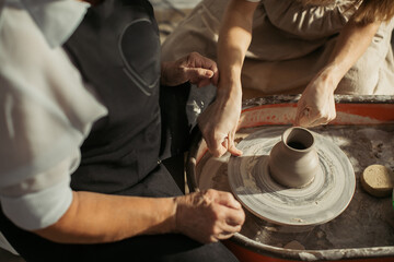 Potter creating clay vase with senior woman on pottery wheel