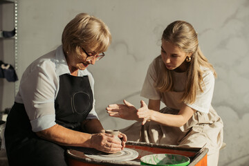 Senior woman learning pottery making with young instructor