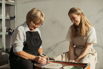 Senior woman learning pottery with young instructor in workshop