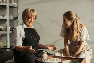 Senior woman learning pottery with young artisan in workshop