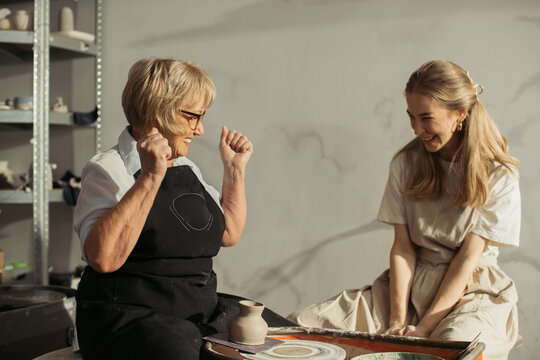 Senior woman celebrating pottery success with instructor - Powered by Adobe