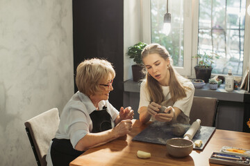 Senior woman learning pottery with young instructor in workshop