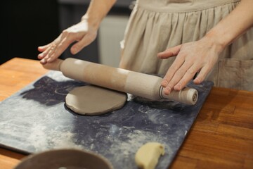 Potter using rolling pin flattening piece of clay on table