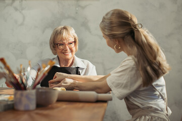 Pottery teacher helping senior woman creating clay vase