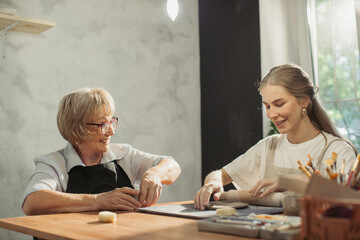 Senior woman learning pottery with young instructor in workshop