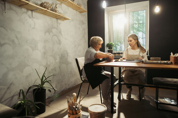 Senior woman learning pottery with young instructor in workshop