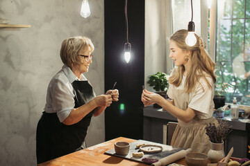 Senior woman learning pottery with young instructor in workshop