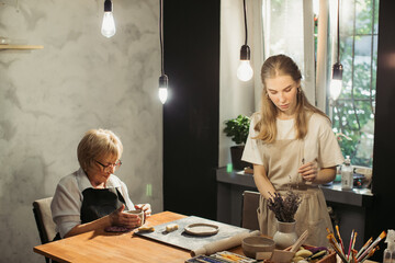 Senior woman learning pottery with young instructor in workshop