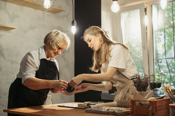 Senior woman learning pottery with young instructor in workshop
