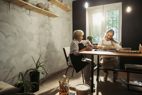 Senior woman learning pottery with young instructor in workshop