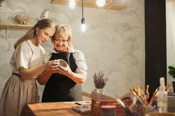 Pottery teacher showing clay vase to senior woman apprentice