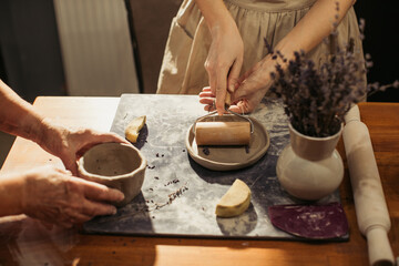 Potter using rolling pin making clay plate with teacher in workshop