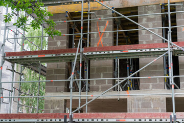 building under construction with metal scaffolding on brick wall marked with orange signs...
