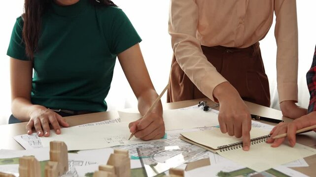 Smart architect and safety engineer discussion about building blueprint on table with architectural document, measurement tools and wooden block scatter around at modern office. Closeup. Delineation.