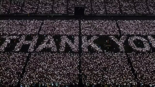 Thank you message in stadium crowd with lights held up at night aerial view
