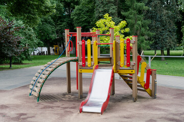 colorful empty children playground with slides climbing net and stairs in public park surrounded by...