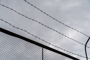 barbed wire fence against cloudy sky symbolizing security restriction prison or border control...