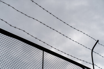 barbed wire fence against cloudy sky symbolizing security restriction prison or border control...