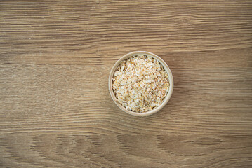 Oat flakes in a light small bowl on a light wooden background