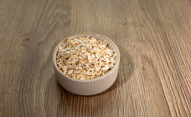 Oat flakes in a light small bowl on a light wooden background