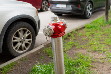 modern street fire hydrant with red metal head and stainless steel body near parked cars on urban...