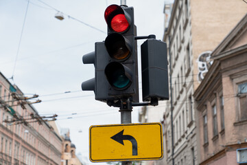 urban traffic light with red signal and left turn arrow road sign on busy street intersection in city center with old architecture buildings electric cables and transportation infrastructure backgroun