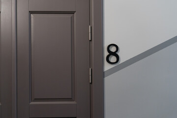 apartment door with number 8 on geometric painted wall, stylish interior entrance with dark brown panel door in modern hallway, minimal residential or hotel corridor design for urban living space