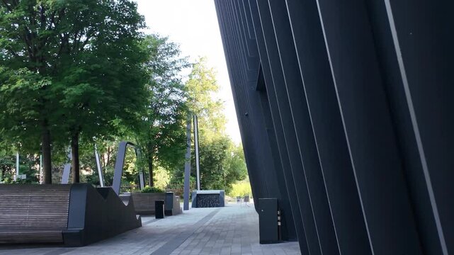 Contemporary pedestrian pathway in Vilnius featuring angled architectural wall, wooden benches, and landscaped greenery under natural daylight.