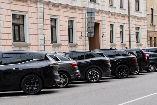 row of modern black parked suvs on city street near beige building facade, urban transportation scene, contemporary cars lined up in residential area, parking in downtown neighborhood