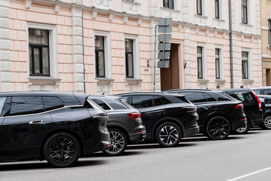row of modern black parked suvs on city street near beige building facade, urban transportation scene, contemporary cars lined up in residential area, parking in downtown neighborhood