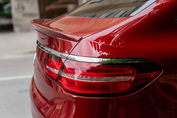 close up of modern red luxury car rear taillight with chrome trim reflecting urban surroundings,...