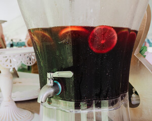 Glass beverage dispenser filled with citrus slices and chilled fruit-infused drink, condensation on...
