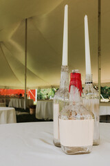 Upcycled glass bottles with dripping red and white wax holding tall taper candles on white...