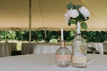 Two upcycled glass bottle centerpieces with dripping white wax taper candles and rose–peony...