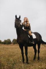Young Woman Riding a Black Horse in a Meadow on a Calm Day